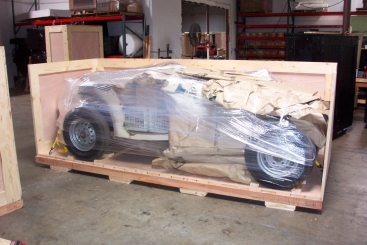 A vehicle in a wooden crate, wrapped in plastic and paper, inside a warehouse.