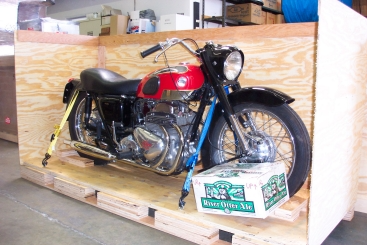 Vintage red and black motorcycle strapped inside a wooden crate, ready for shipping.
