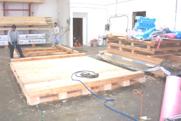 Two men assembling a large wooden pallet in a warehouse.