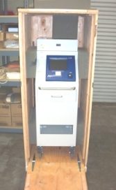 A medical device in a wooden shipping crate, on wheels, with a control panel and screen.
