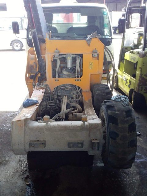 Yellow and white backhoe with a cab and large tires, parked inside a garage.