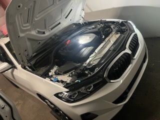 White BMW sedan with hood open, engine visible.