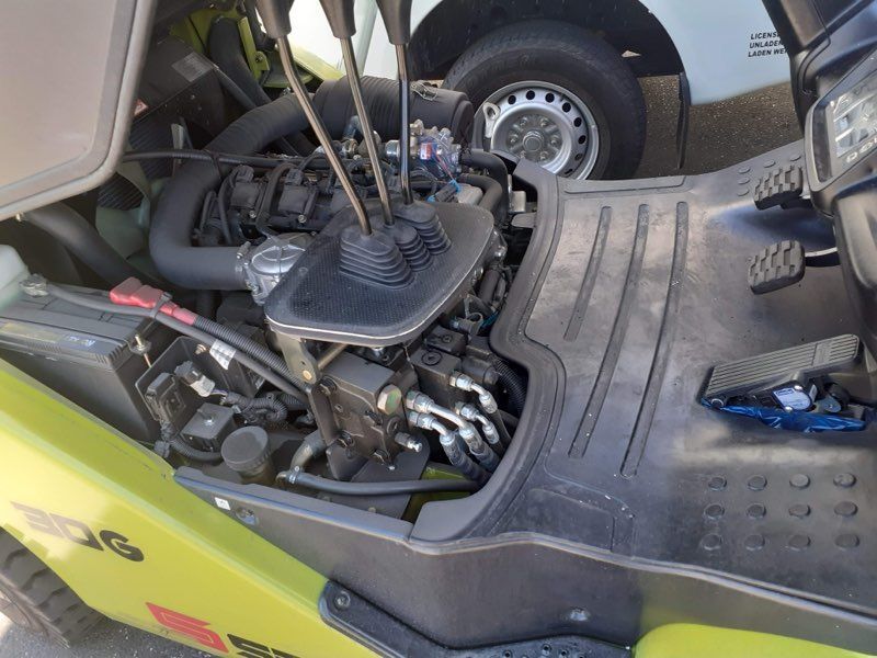 Forklift engine compartment, black and silver components, with control levers. Yellow forklift exterior visible.