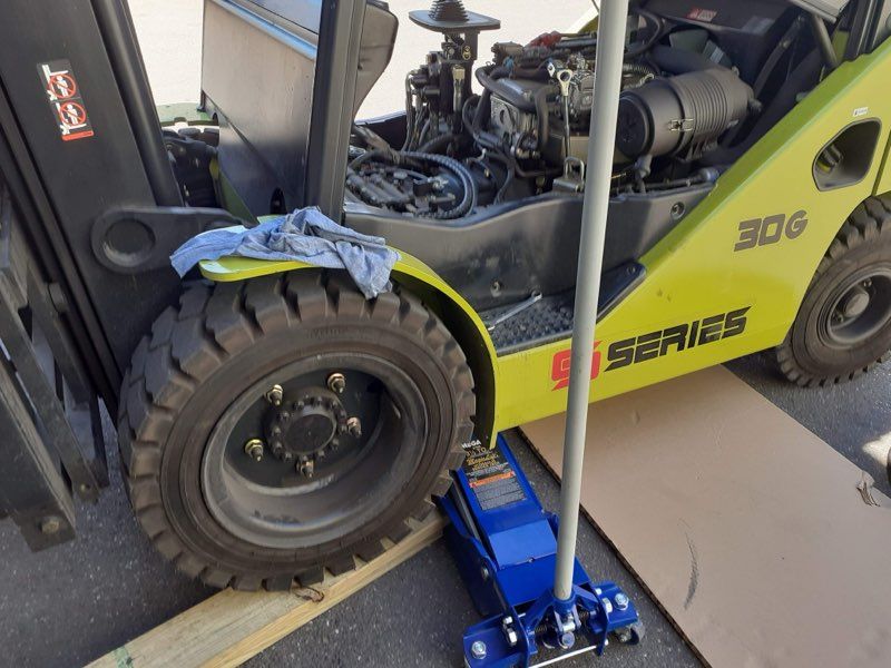 Forklift with open engine compartment, jacked up on a blue jack, outdoors.