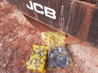 JCB construction equipment with two yellow-wrapped parts on red dirt ground.