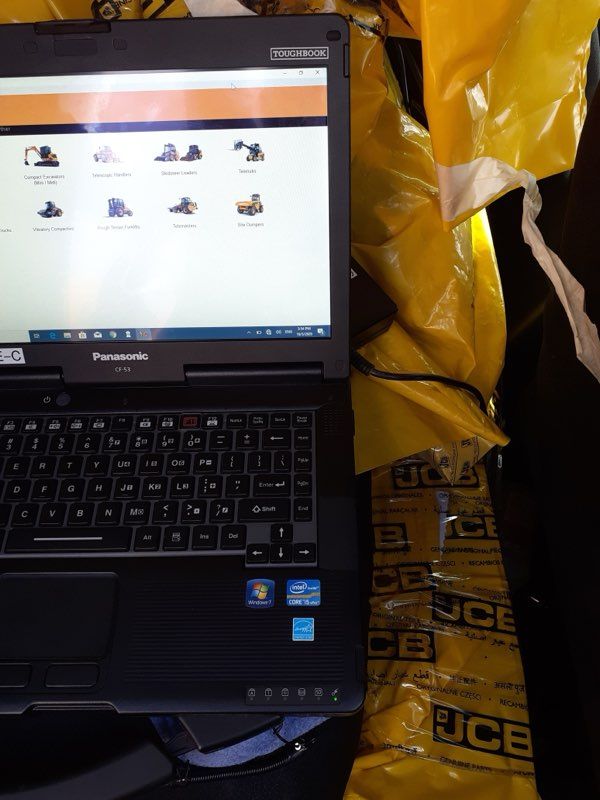 Laptop displaying diagnostic software, next to yellow JCB bags.