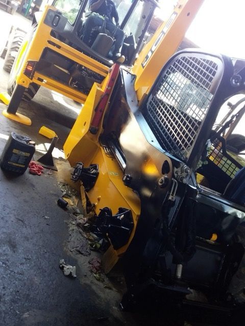 Yellow skid steer and backhoe parked indoors; a person in the backhoe.