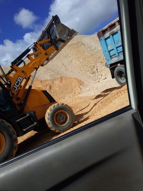 Yellow JCB loader filling a blue truck with tan material on a sunny day.