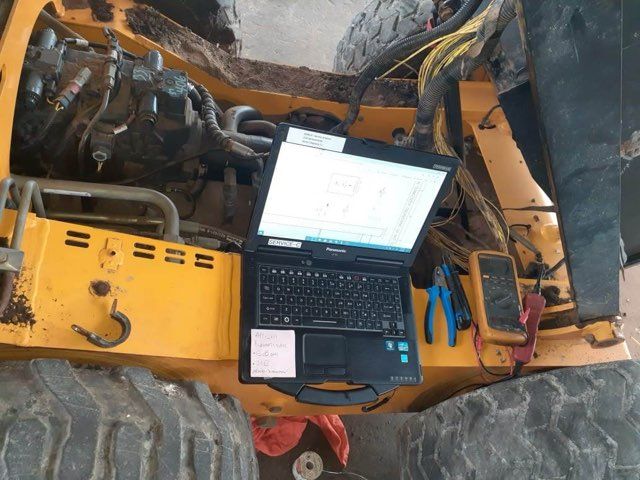 Laptop on a yellow machine, diagnostic work in progress. Tools visible.