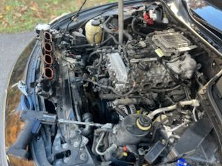 Car engine bay with intake manifold removed, mid-repair, tools present.