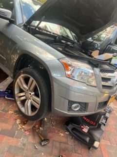 Silver SUV with hood open, being worked on. Oil drain pan is visible beneath the vehicle.