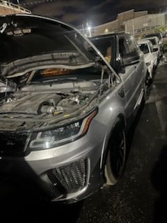 Silver Range Rover with hood open, parked on a street at night.