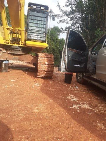 Yellow excavator next to a car with an open door on a dirt road.