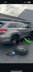 A gray SUV has a wheel removed. It's supported by a jack and stands, with a spare tire and tools on the ground.