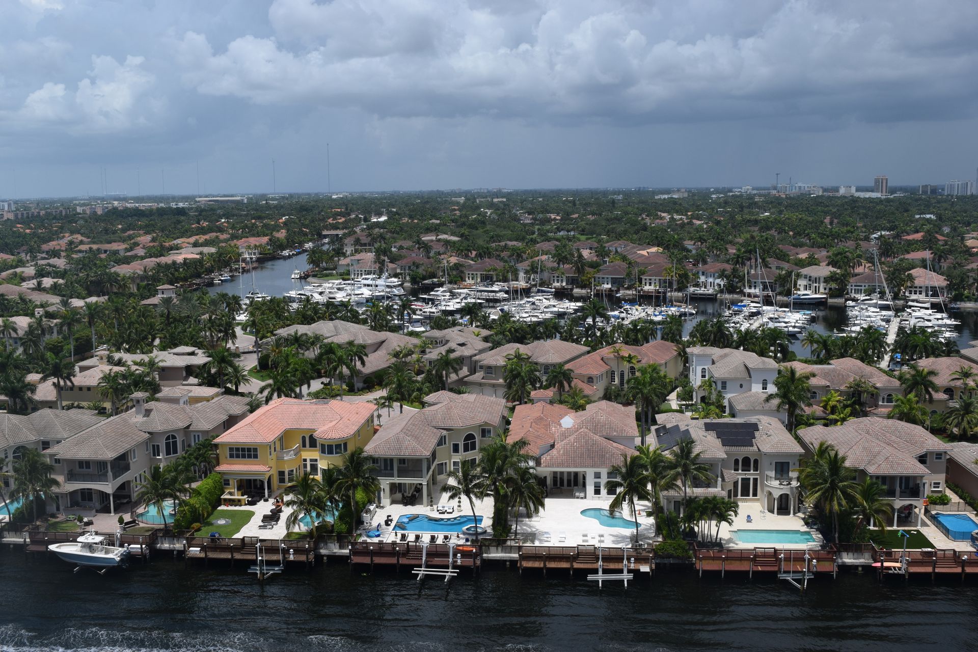Aerial view of waterfront houses with private docks, swimming pools, and boats along a canal in a suburban neighborhood.