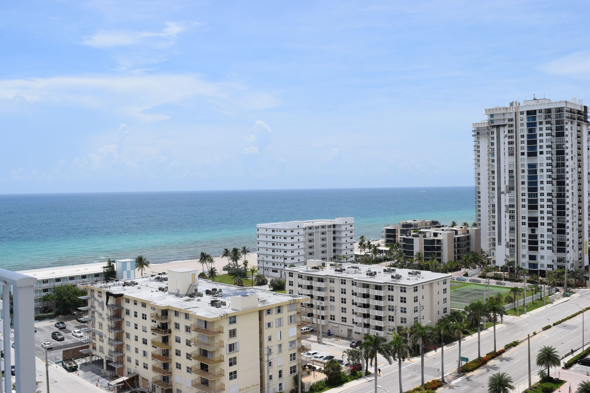 A coastal cityscape featuring several apartment buildings near a sandy beach and the blue ocean under a clear sky.