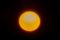 A bright, glowing yellow sun set against a solid black background, featuring small dark sunspots near its center.