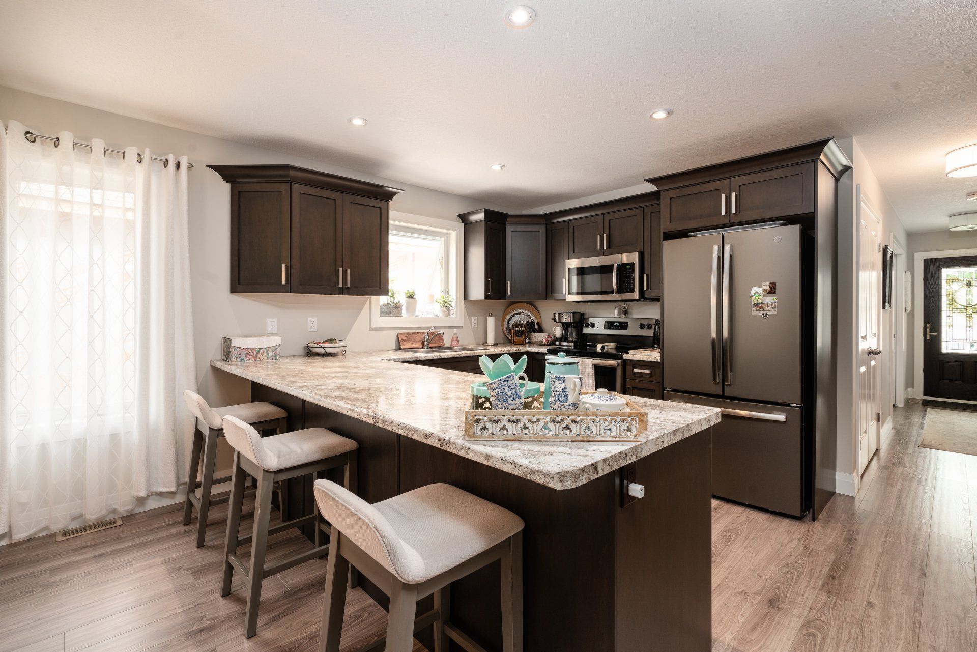A kitchen with a large island , stools , a refrigerator and a microwave.