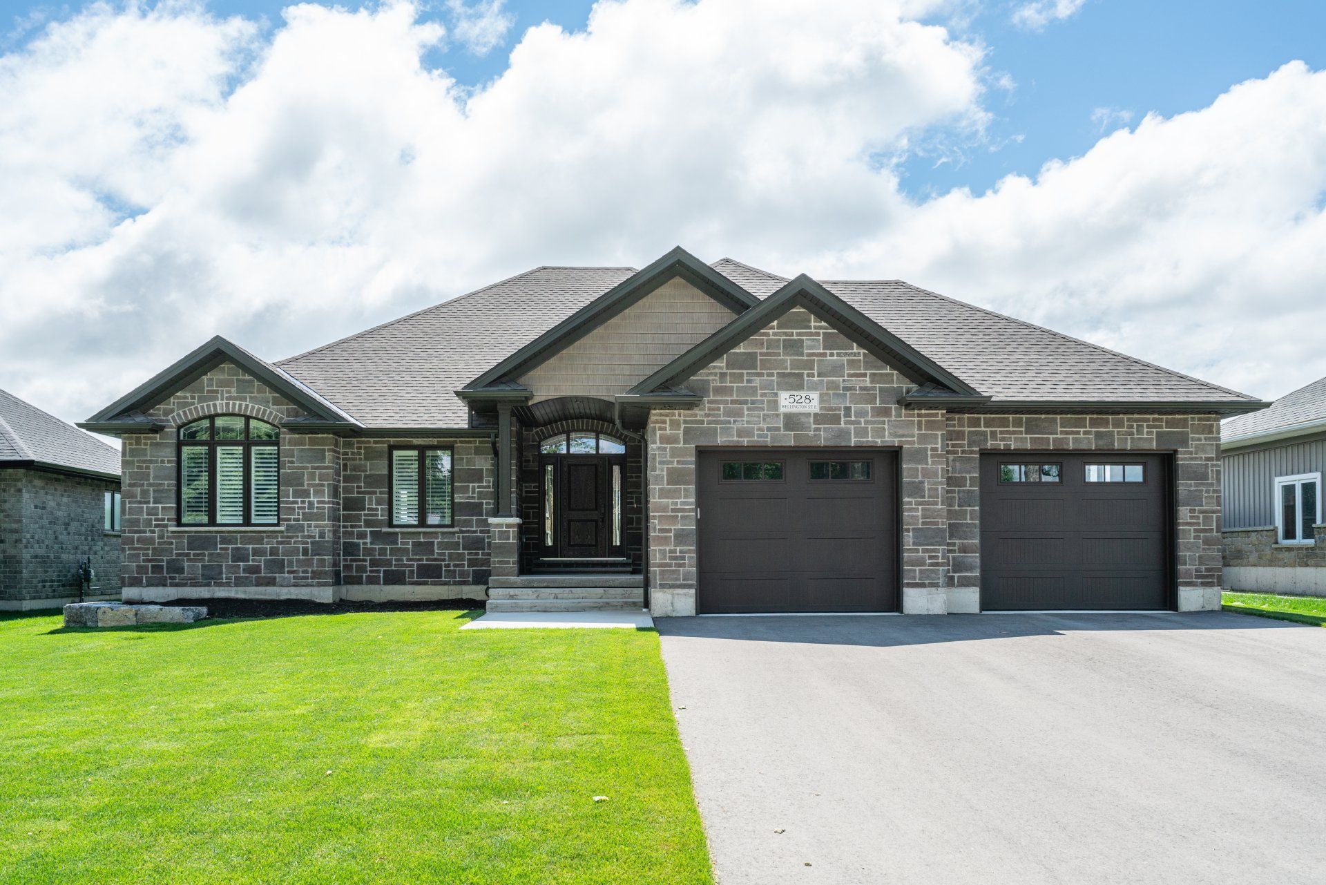 A large brick house with two garage doors is sitting on top of a lush green lawn.