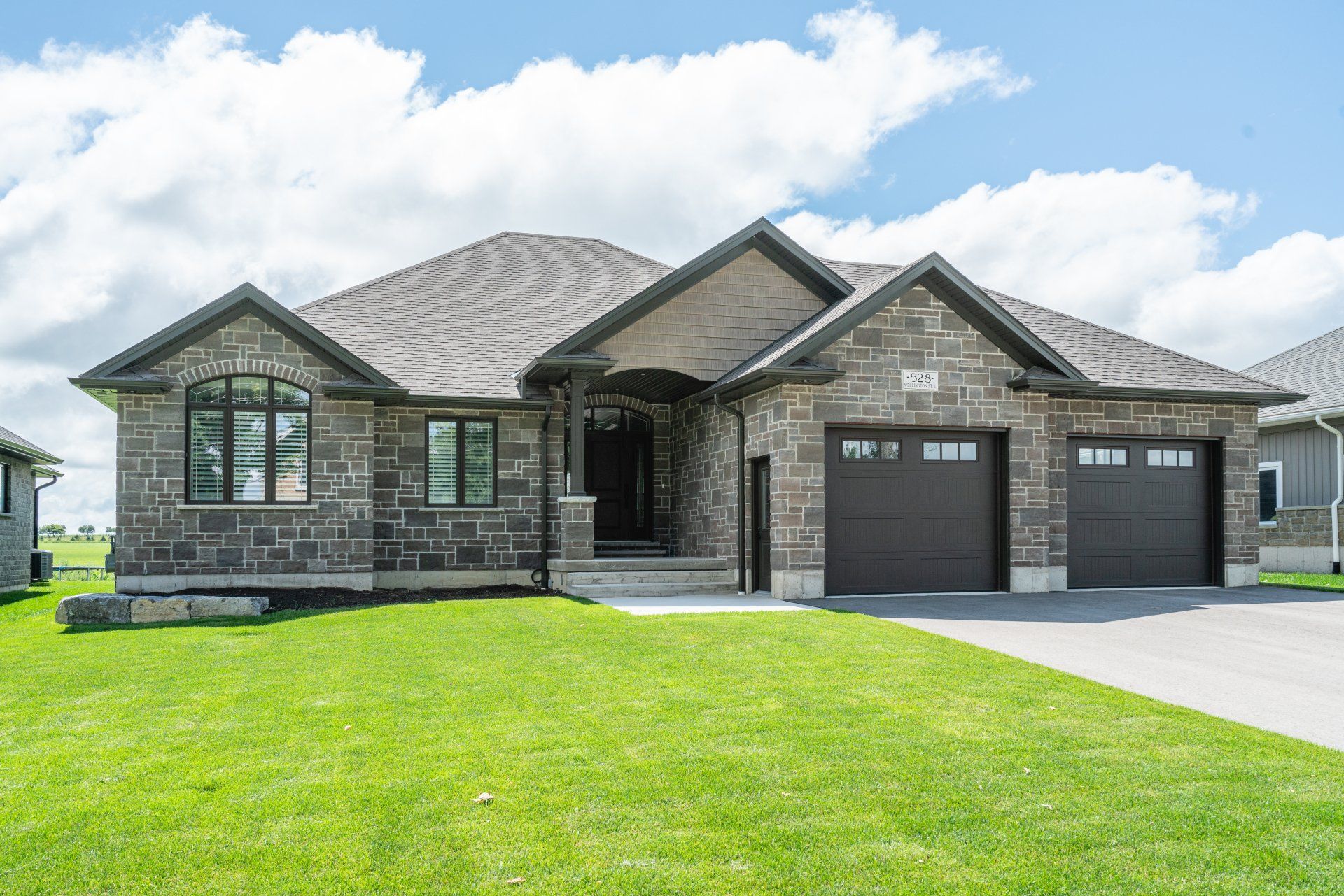 A large stone house with two garages and a lush green lawn in front of it.