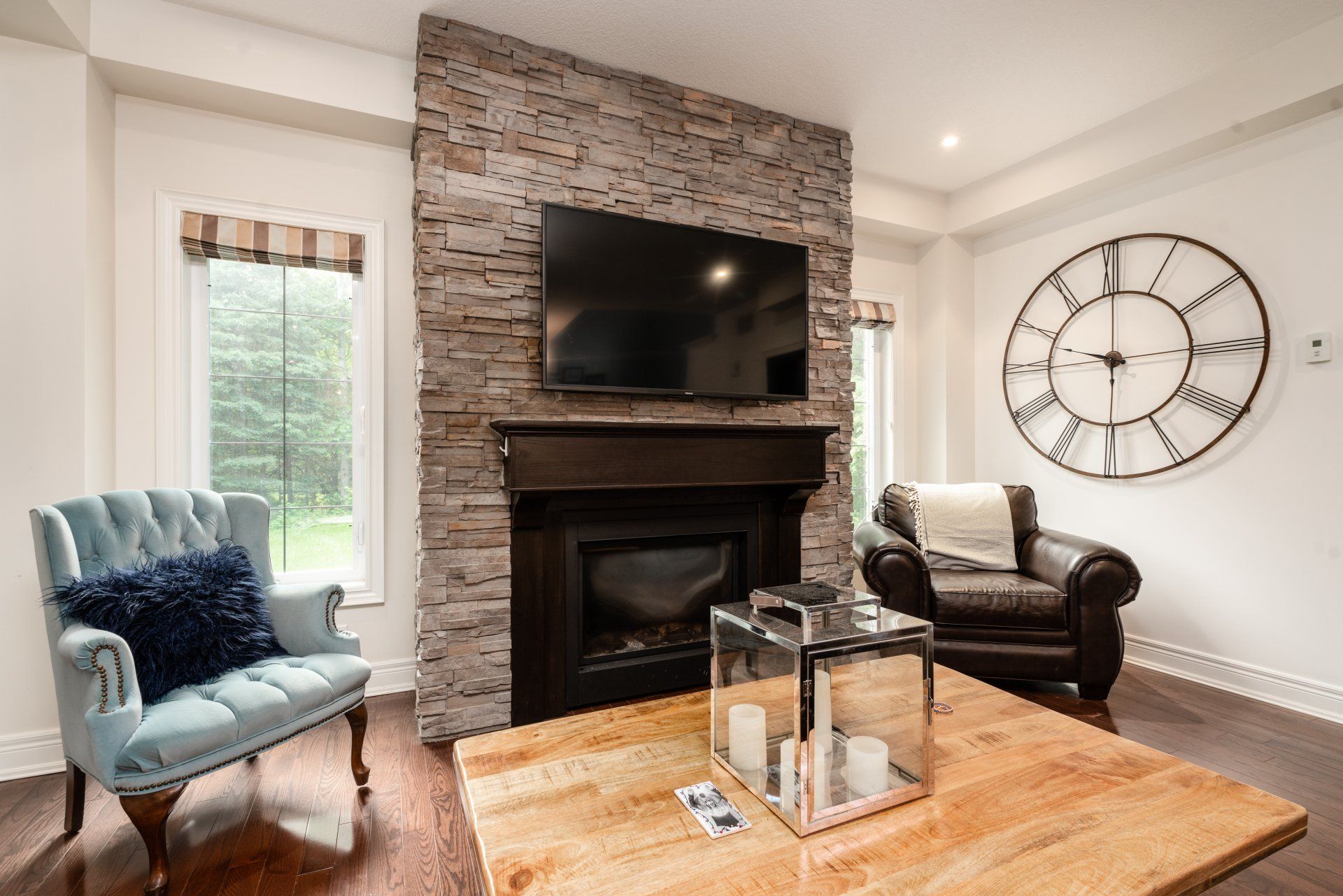 A living room with a fireplace , television , chairs and a clock on the wall.
