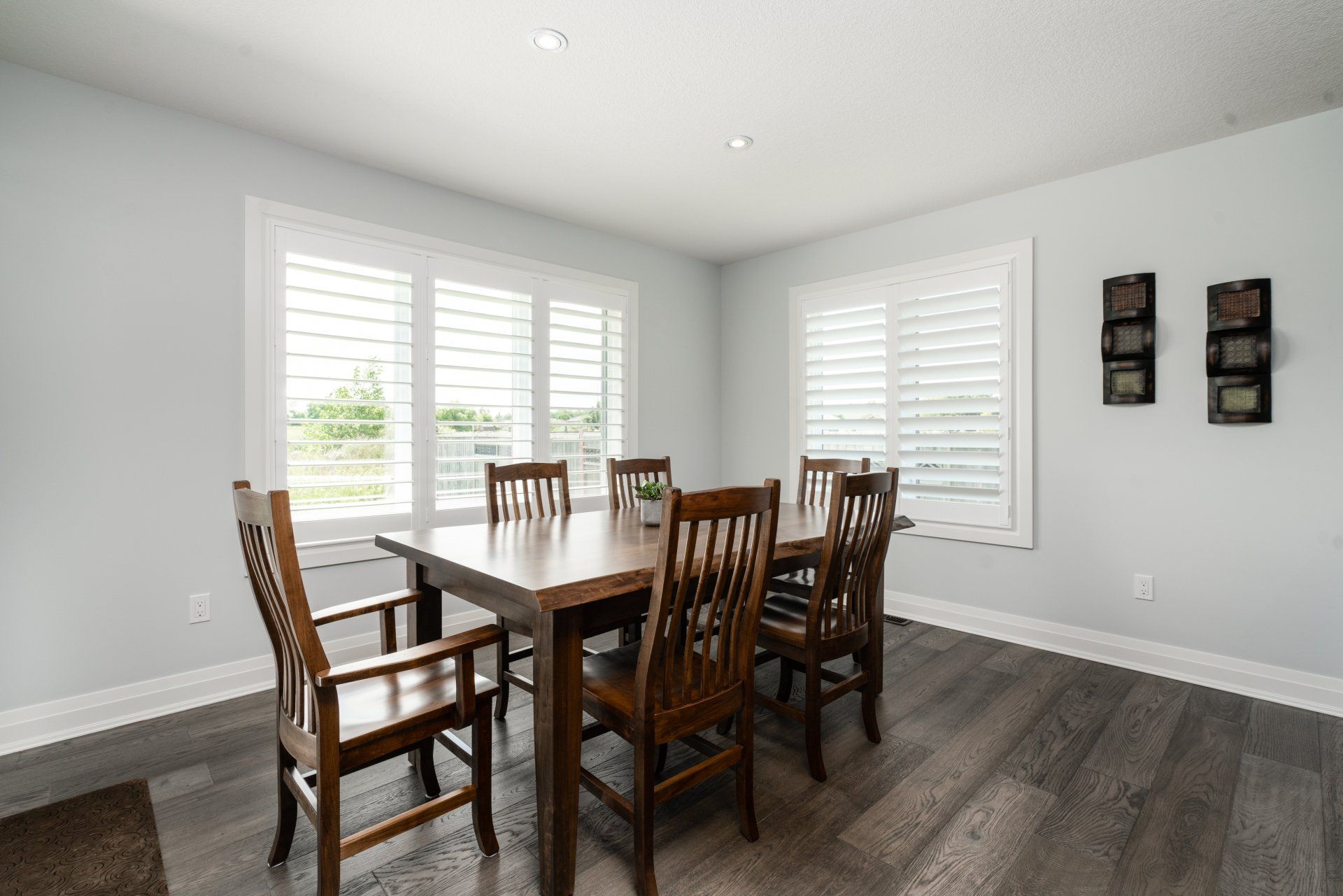 A dining room with a table and chairs and shutters on the windows.