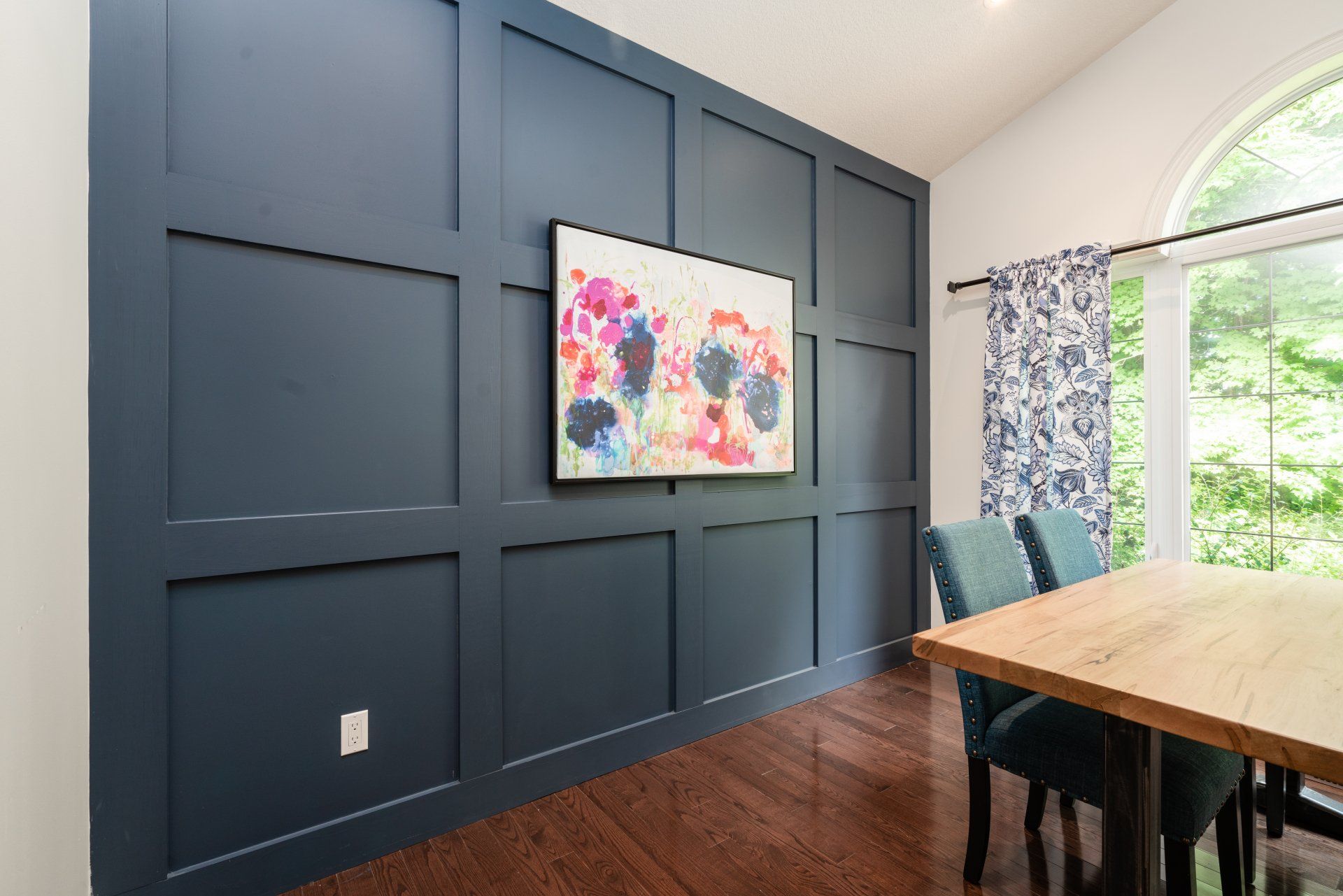 A dining room with a table and chairs and a painting on the wall.