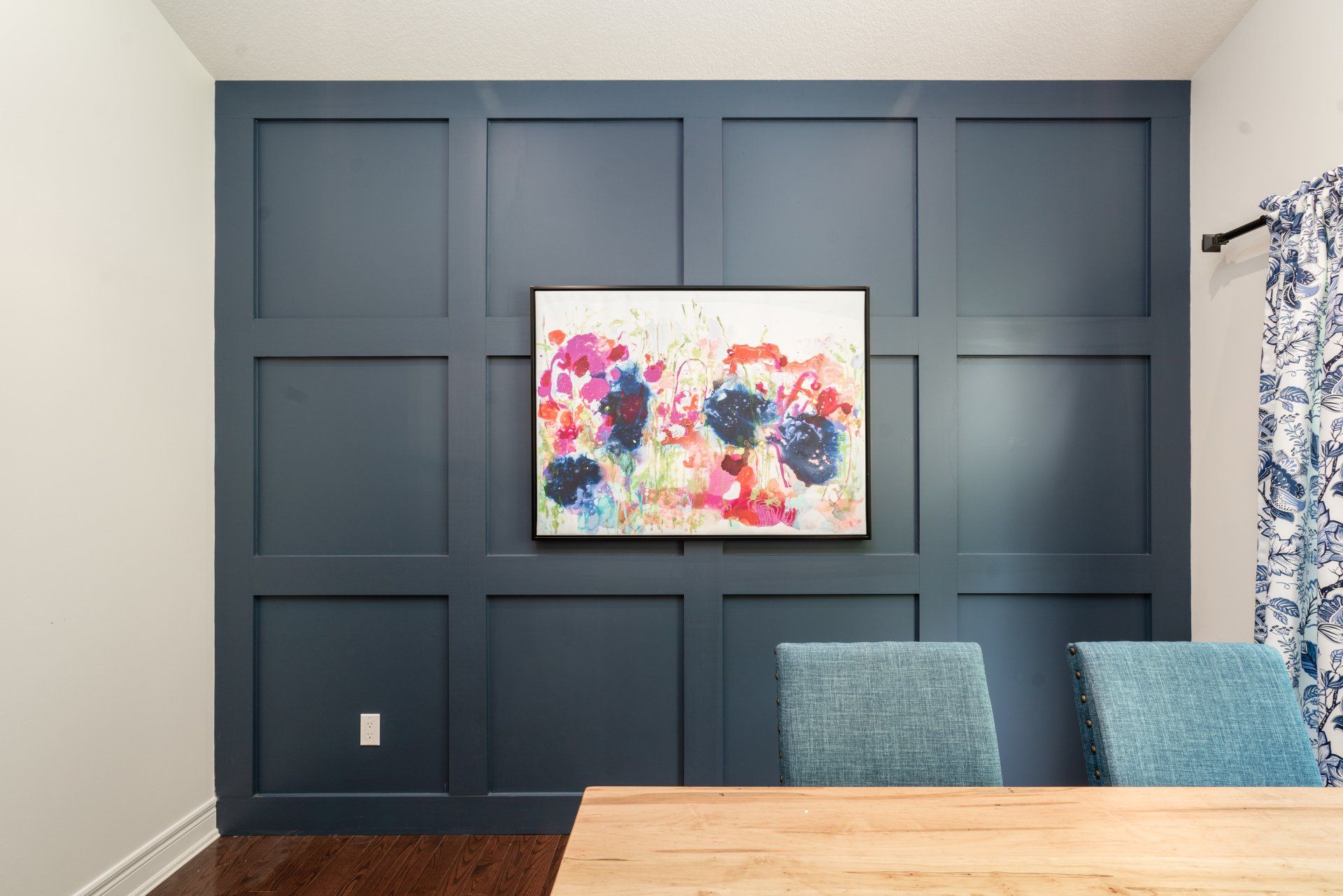A dining room with a table and chairs and a painting on the wall.