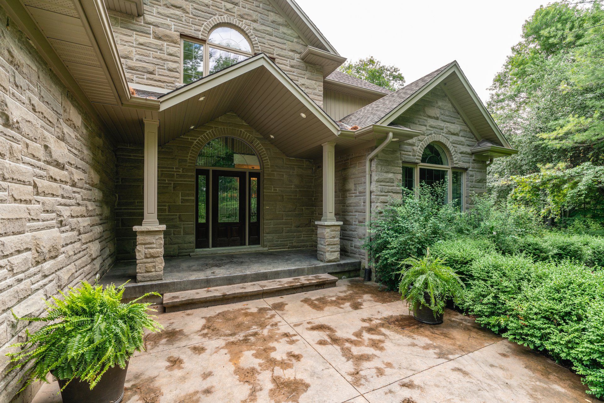 A large stone house with a porch and a patio in front of it.