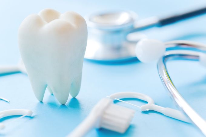 Concetto di salute dentale con un dente bianco, uno stetoscopio e uno spazzolino da denti su sfondo blu.