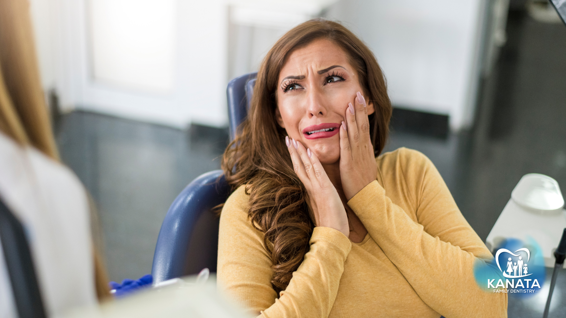 A woman is sitting in a dental chair with her hands on her face.