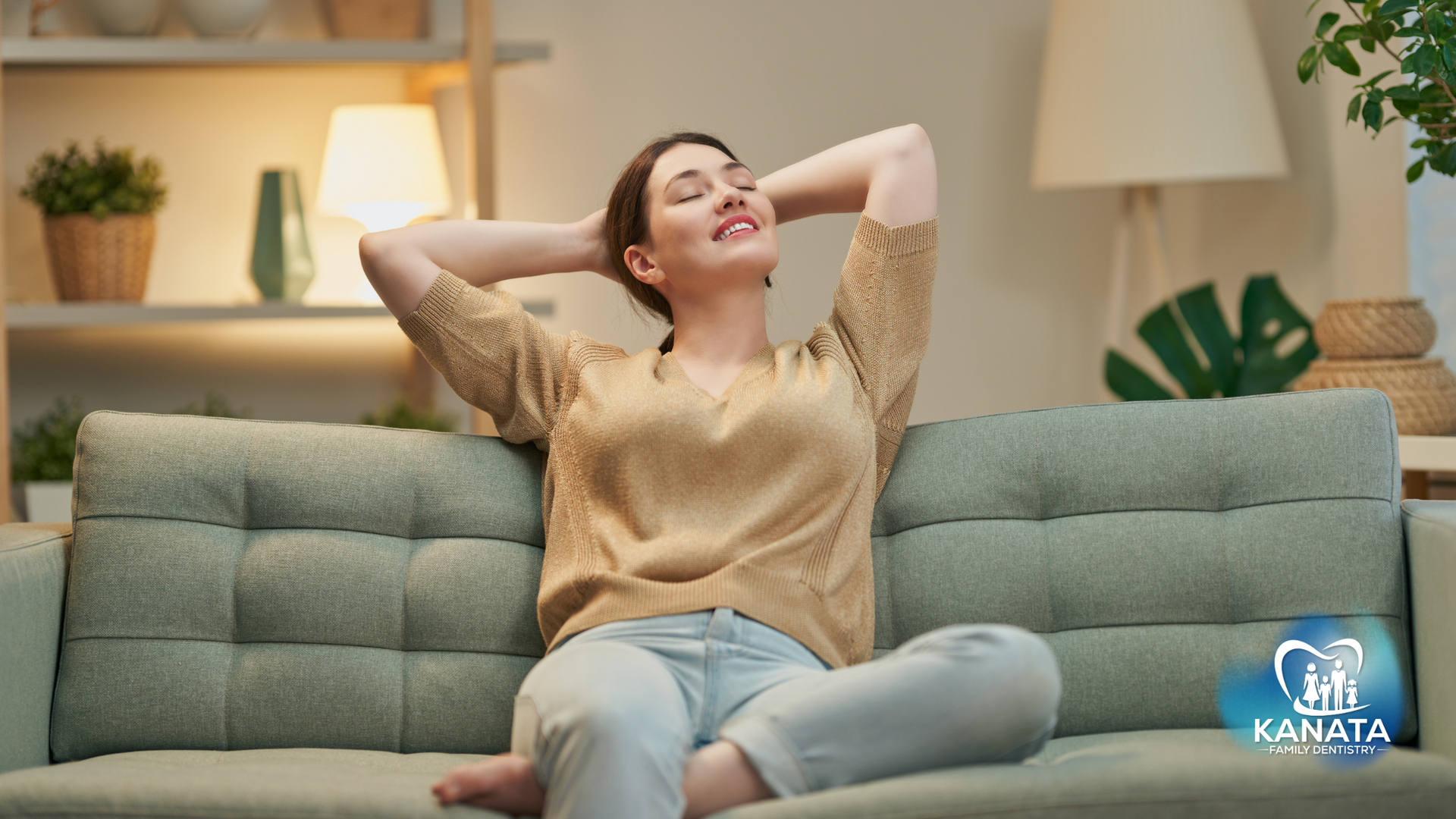 A woman is sitting on a couch with her hands behind her head.