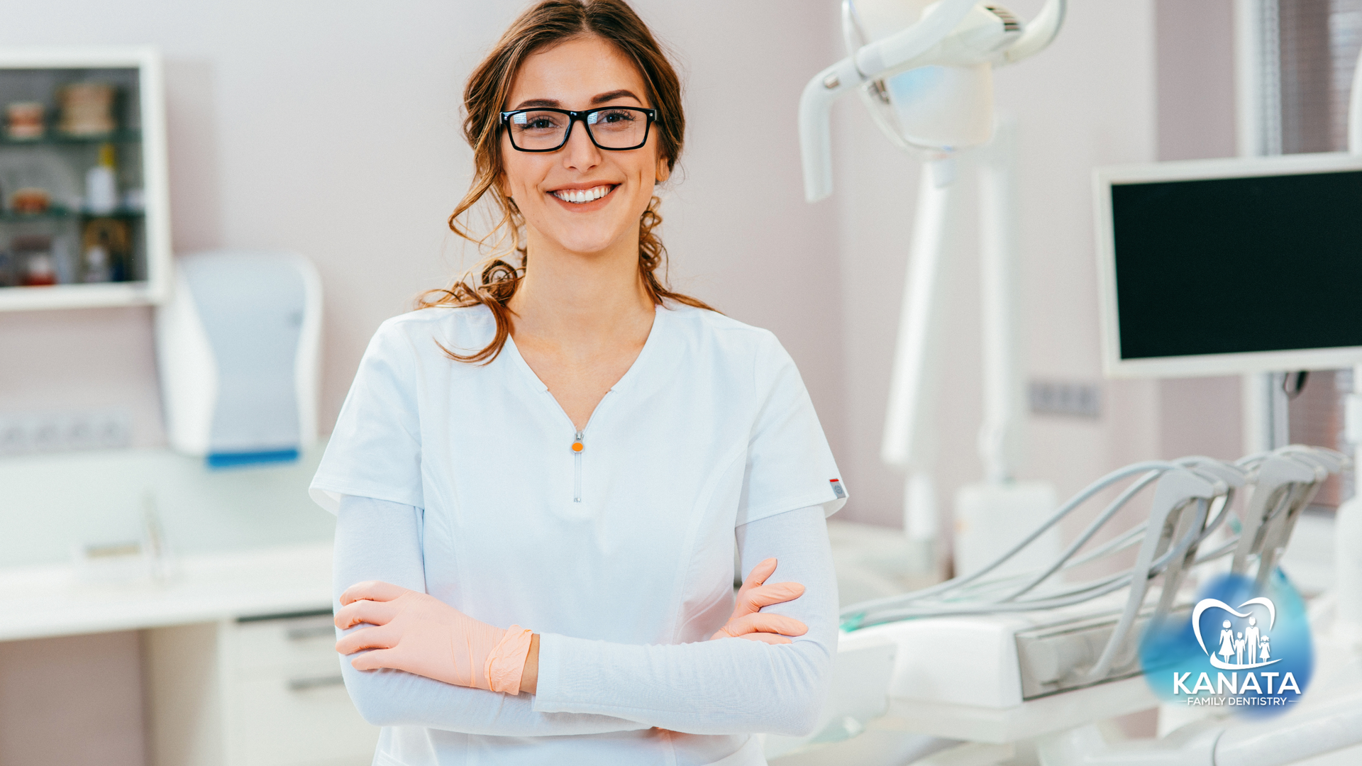 A female dentist is standing in a dental office with her arms crossed and smiling.