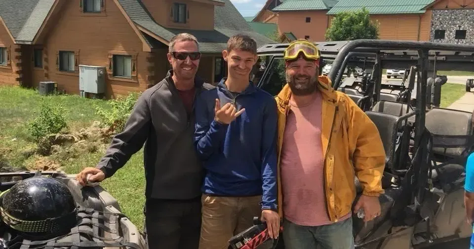 Three men are posing for a picture in front of a atv.