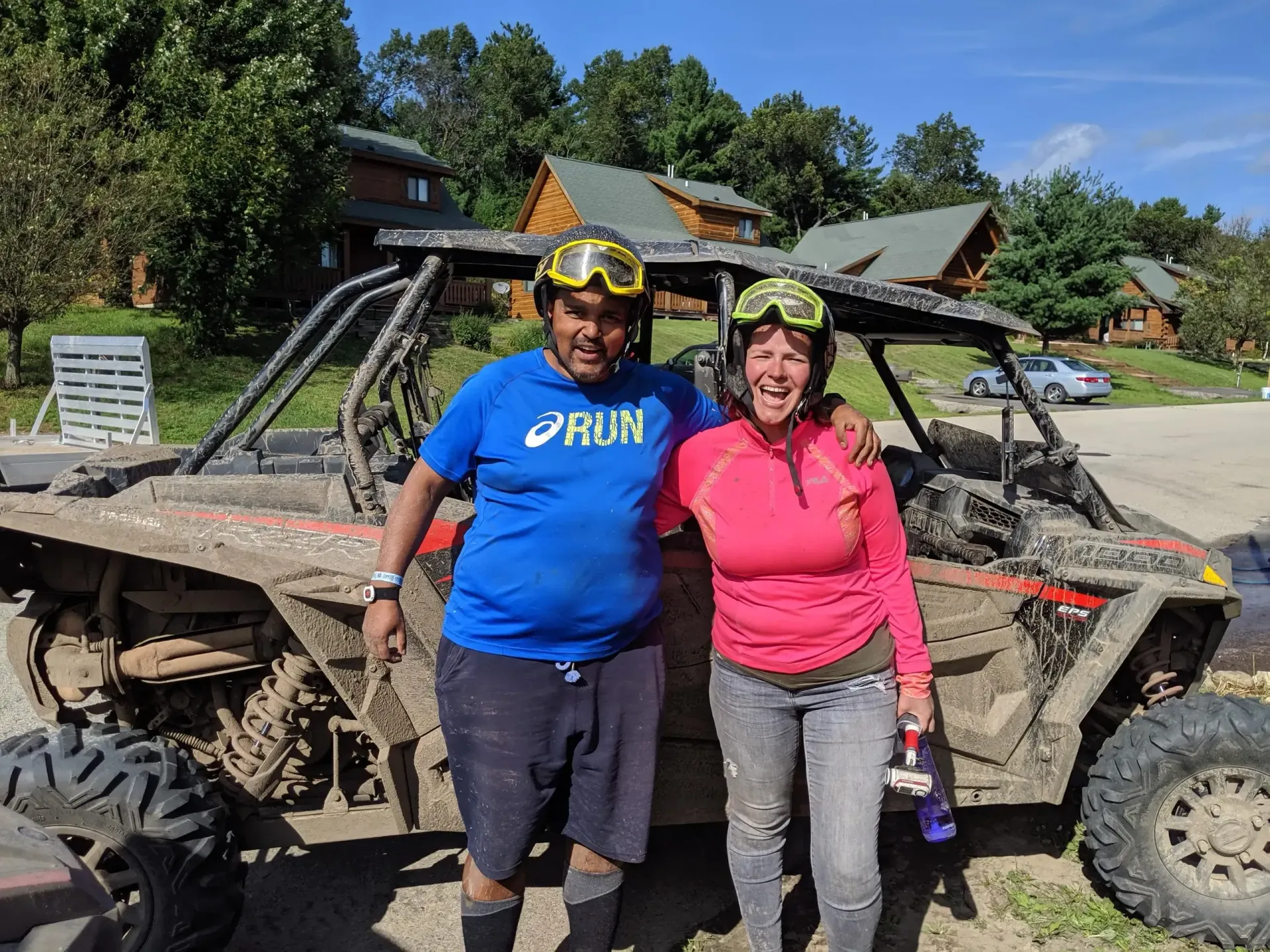 A man and a woman are posing for a picture in front of a muddy atv.