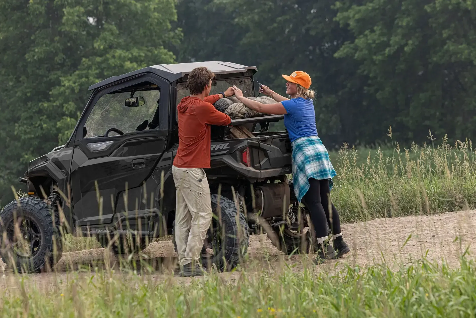 A man and a woman are pushing a atv down a dirt road.