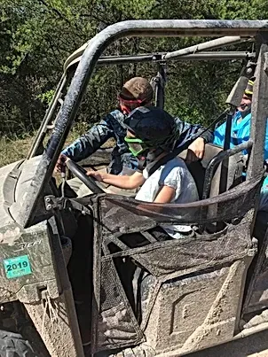 A man and a girl are sitting in a muddy atv.