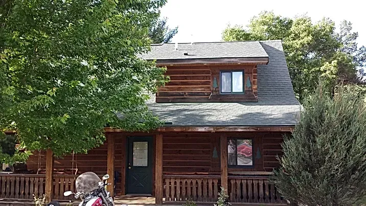 A man is riding a motorcycle in front of a log cabin.