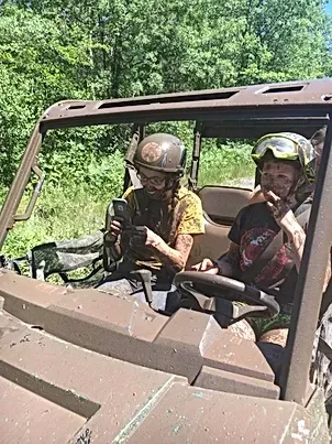 A man and a boy are sitting in a muddy atv.