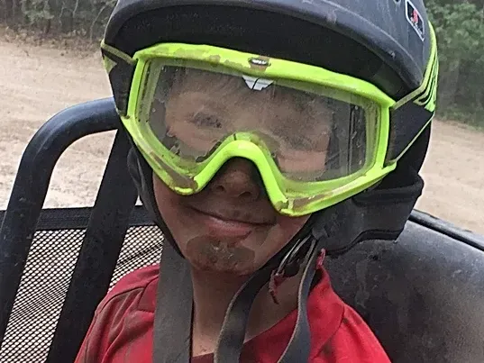 A young boy wearing a helmet and goggles is sitting in a vehicle.