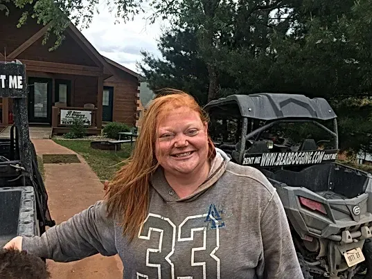A woman is standing in front of two atvs and smiling.