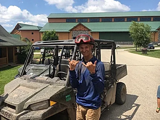 A young man wearing a helmet and goggles is standing next to a atv.