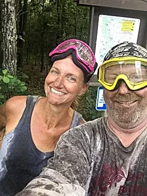A man and a woman wearing goggles are taking a selfie in the woods.