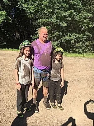 A man and two children are standing next to each other in a dirt field.