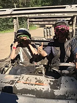Two people are sitting in a vehicle giving a thumbs up.