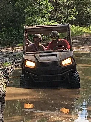 Two people are riding a polaris rzr in the mud.