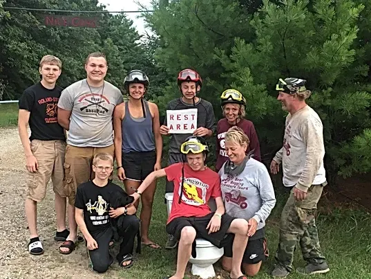 A group of people are posing for a picture with a boy sitting on a toilet.
