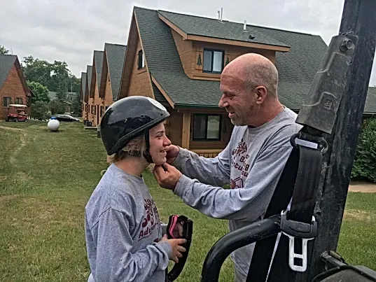 A man is helping a young girl put on a helmet.