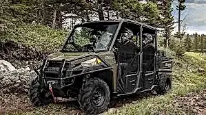A green atv is parked on a dirt road in the woods.