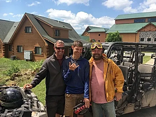 Three men are posing for a picture in front of a atv.